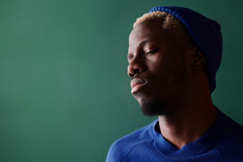 Free Serene portrait of a man with closed eyes and a blue hat, against a green background, expressing calm and relaxation. Stock Photo