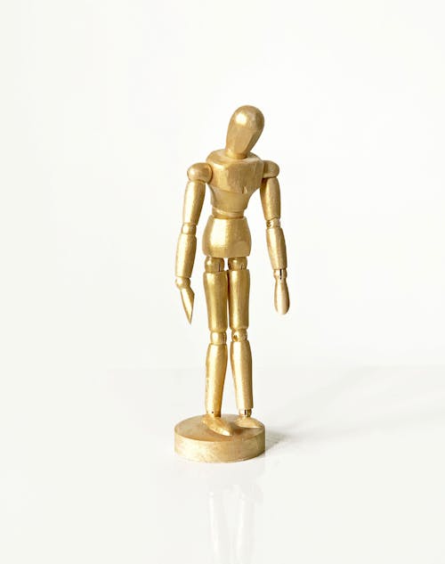 Close-Up Shot of a Gold Wooden Figurine on a White Surface