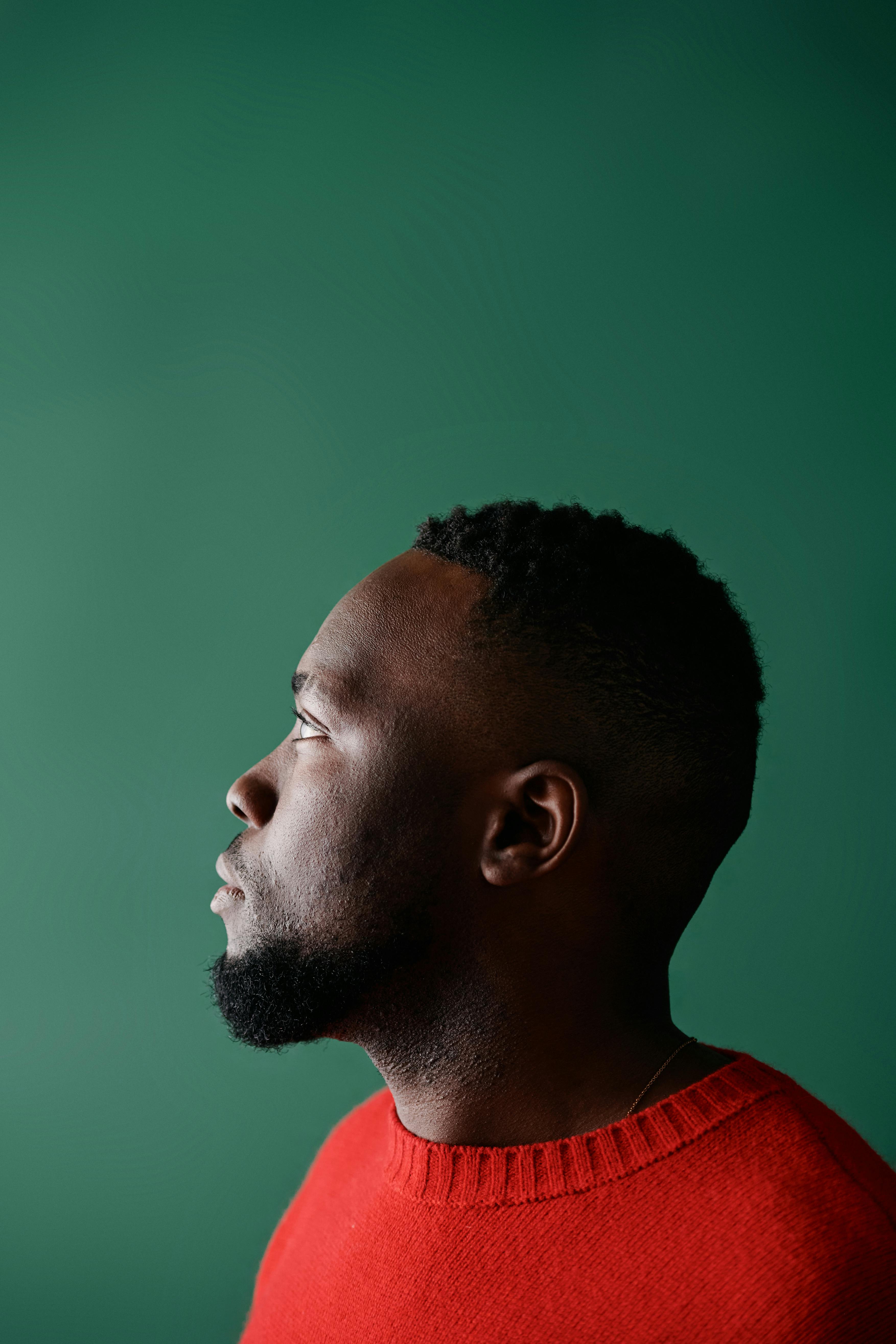Profile of a man in a red sweater against a green backdrop, showcasing thoughtful expression.
