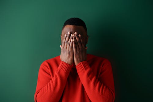 A Man Wearing a Red Sweater Covering His Face with His Hands