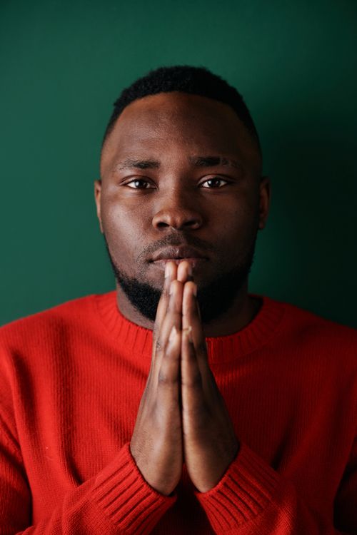 Free Thoughtful portrait of a man in a red sweater posing with praying hands against a green background. Stock Photo