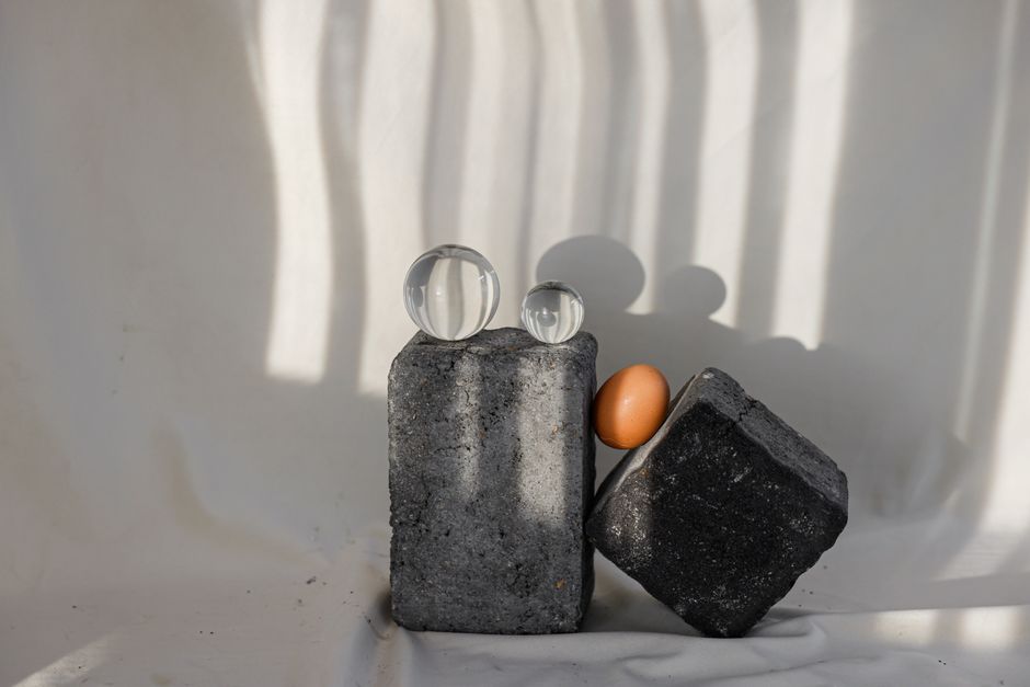 Artistic abstract composition of stone blocks, egg, and glass spheres with dramatic shadows.