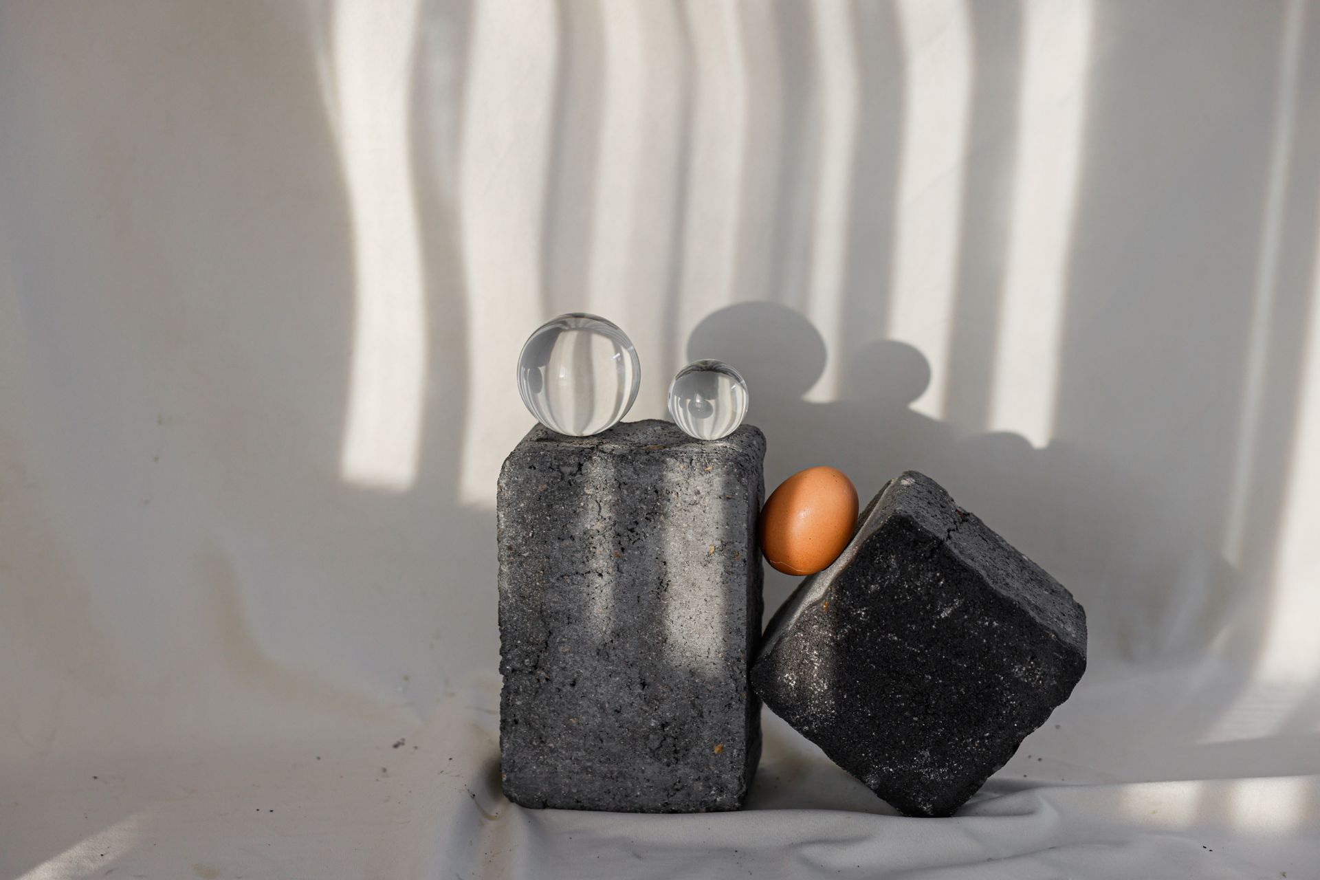 Artistic abstract composition of stone blocks, egg, and glass spheres with dramatic shadows.