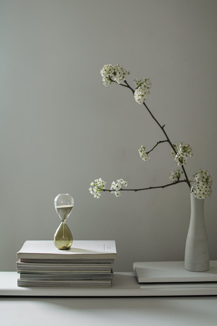 A Flower Vase And Hourglass Over Books