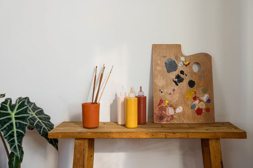 Free A painter's workspace with a wooden palette, paintbrushes, and art supplies on a rustic table. Stock Photo