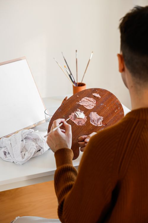 Free Artist using a palette to mix colors in a bright studio setting. Creative over-the-shoulder view. Stock Photo