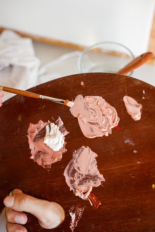 Free Close-up of an artist's hand mixing paints on a wooden palette with a brush. Stock Photo