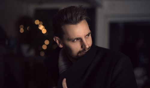 Free Portrait of a handsome man in a coat indoors with creative lighting and bokeh effect. Stock Photo