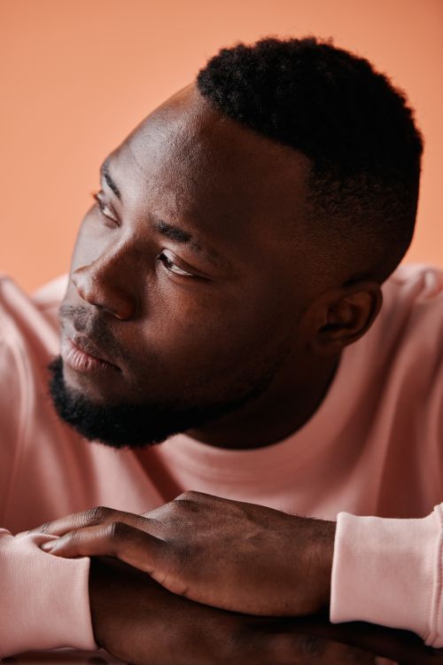 Free Close-up portrait of a thoughtful young man in a pink sweater against a warm background. Stock Photo