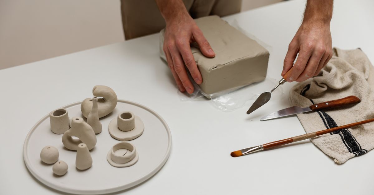 Close-up of hands sculpting clay with tools in a studio setting.