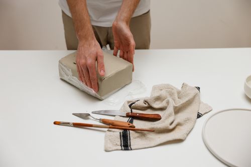 Free Hands preparing clay with tools on a table, ready for sculpting. Stock Photo