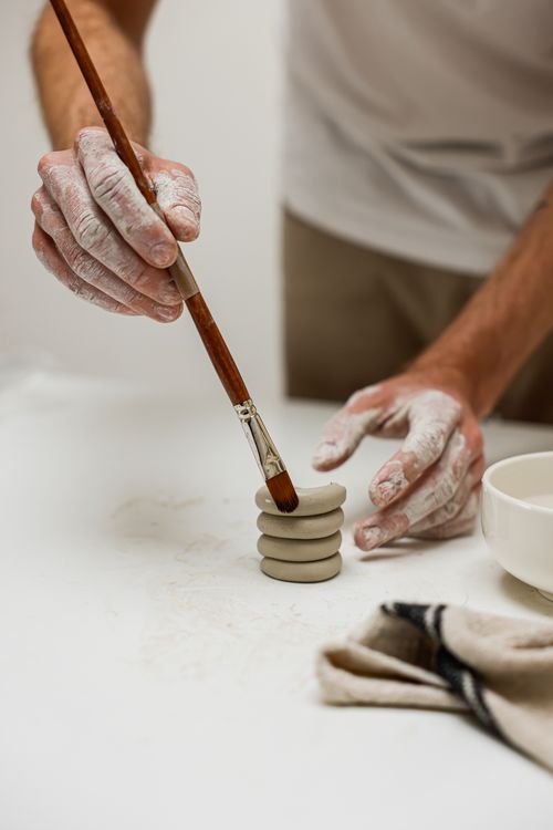 Free Hands working on painting clay pieces with a paintbrush at a crafting table. Stock Photo