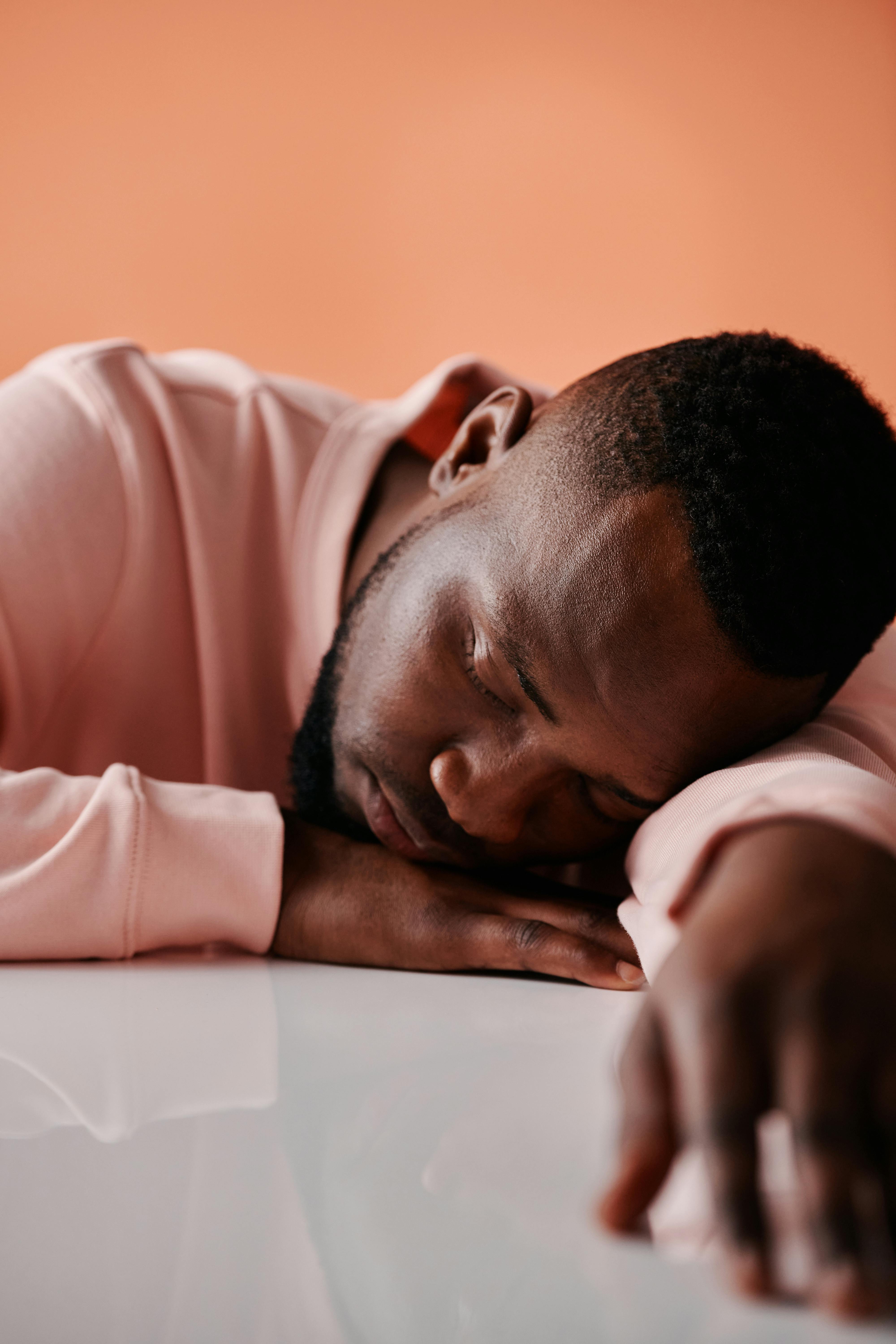 Close-up of an adult black man peacefully resting on a table, wearing a pink sweater.
