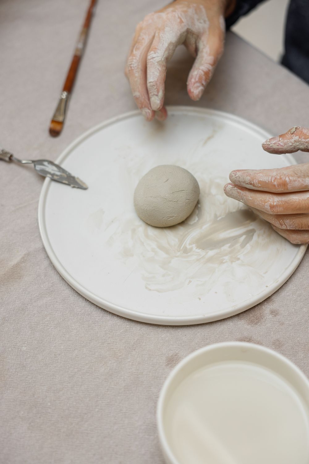 Hands pressing fresh clay on a studio worktable