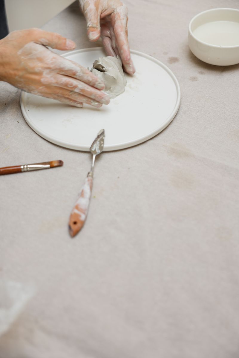 Hands painting glaze onto a leather-hard clay cup