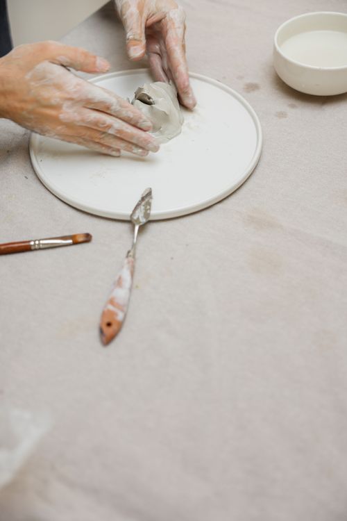 Free Close-up of hands molding clay on a potter's wheel with tools nearby. Stock Photo