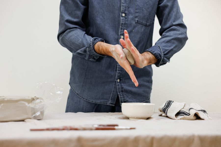 Hands shaping a small clay form at a workbench — photo by Cup of Couple on Pexels