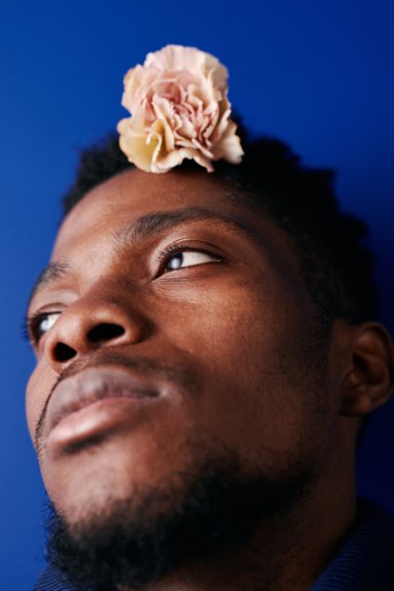 Creative portrait of a bearded man with a flower on blue background.