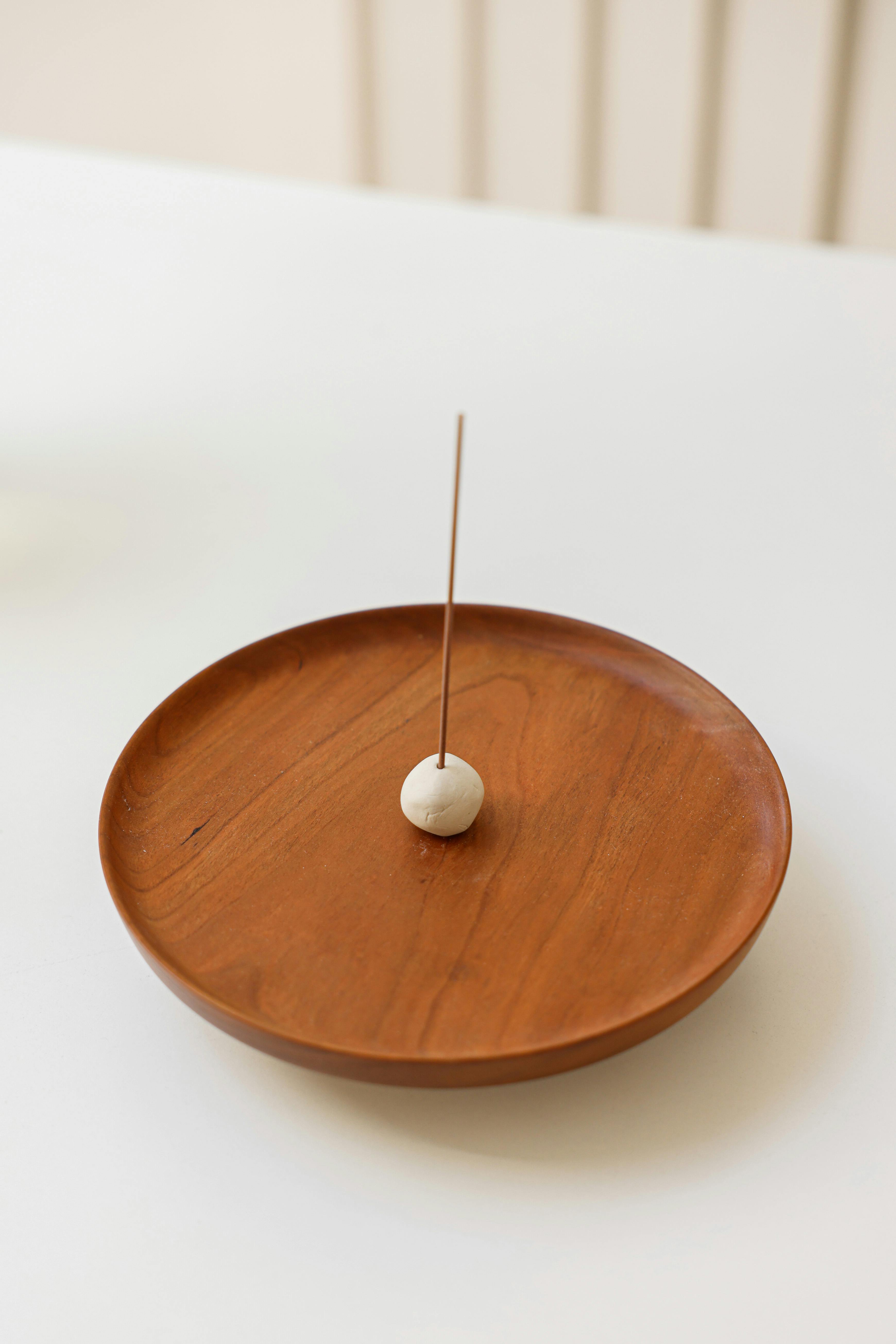A single incense stick elegantly placed on a wooden plate, creating a calm, minimalist vibe.