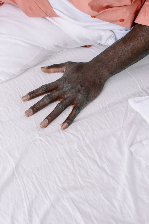 Free A detailed photograph of a person's hand resting on crisp white bed sheets. Stock Photo