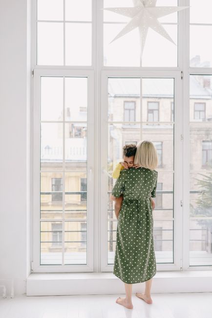 A tender moment of a mother holding her child indoors by a large window.