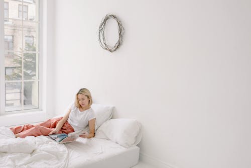 Woman Lying in Bed and Looking Through a Magazine 