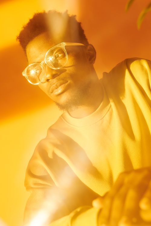 Free Artistic portrait of a young man wearing eyeglasses in a vibrant yellow setting with lens flare effects. Stock Photo