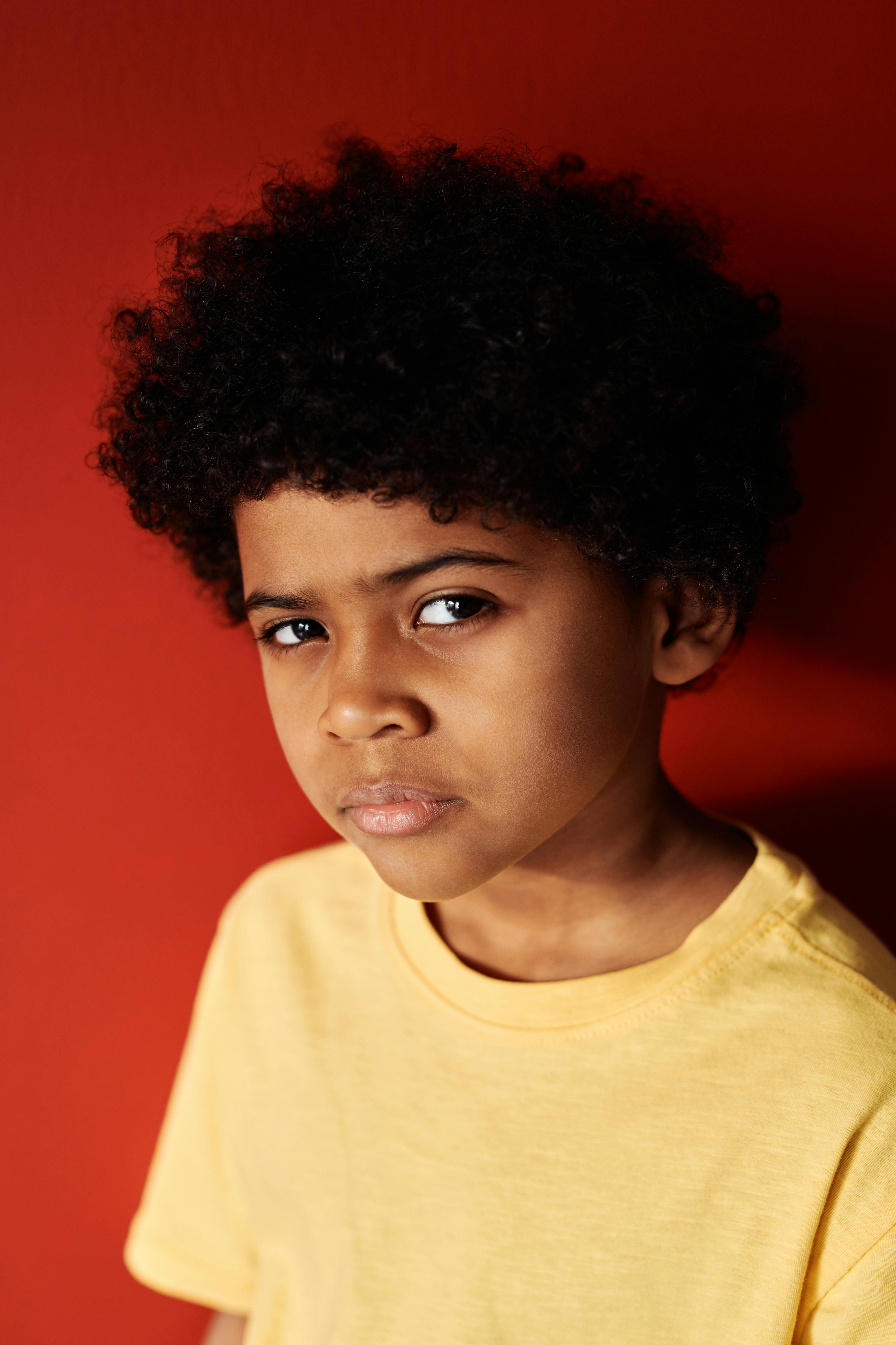 Portrait of a young boy with curly hair wearing a yellow shirt against a red background.