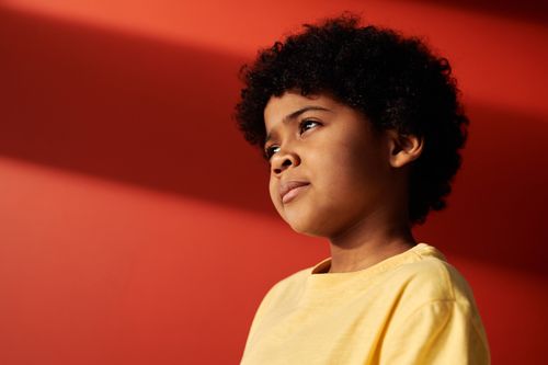 Free Adorable portrait of a young boy with curly hair in a yellow shirt against a red backdrop. Stock Photo