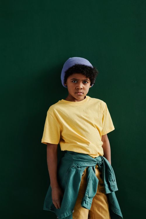 Free Young child poses confidently in a yellow shirt with trendy accessories on a solid green background. Stock Photo