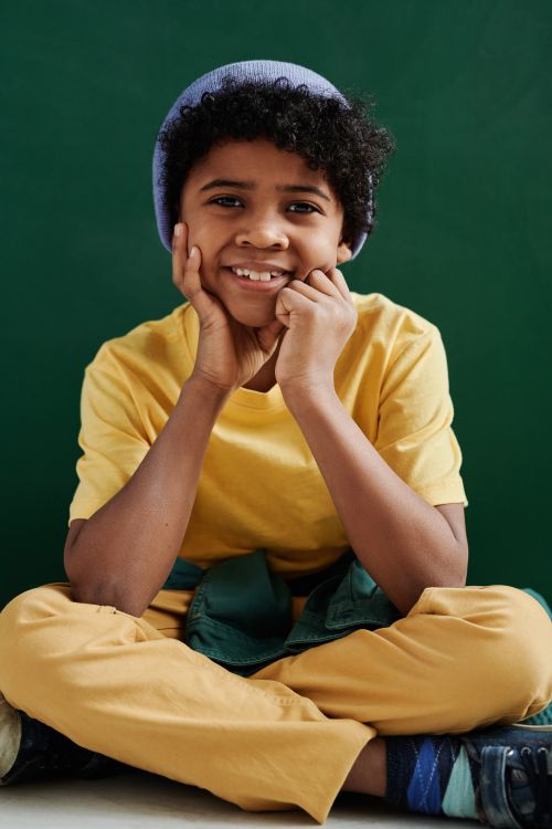 Free Smiling child in a yellow outfit sitting indoors, exuding warmth and happiness. Stock Photo