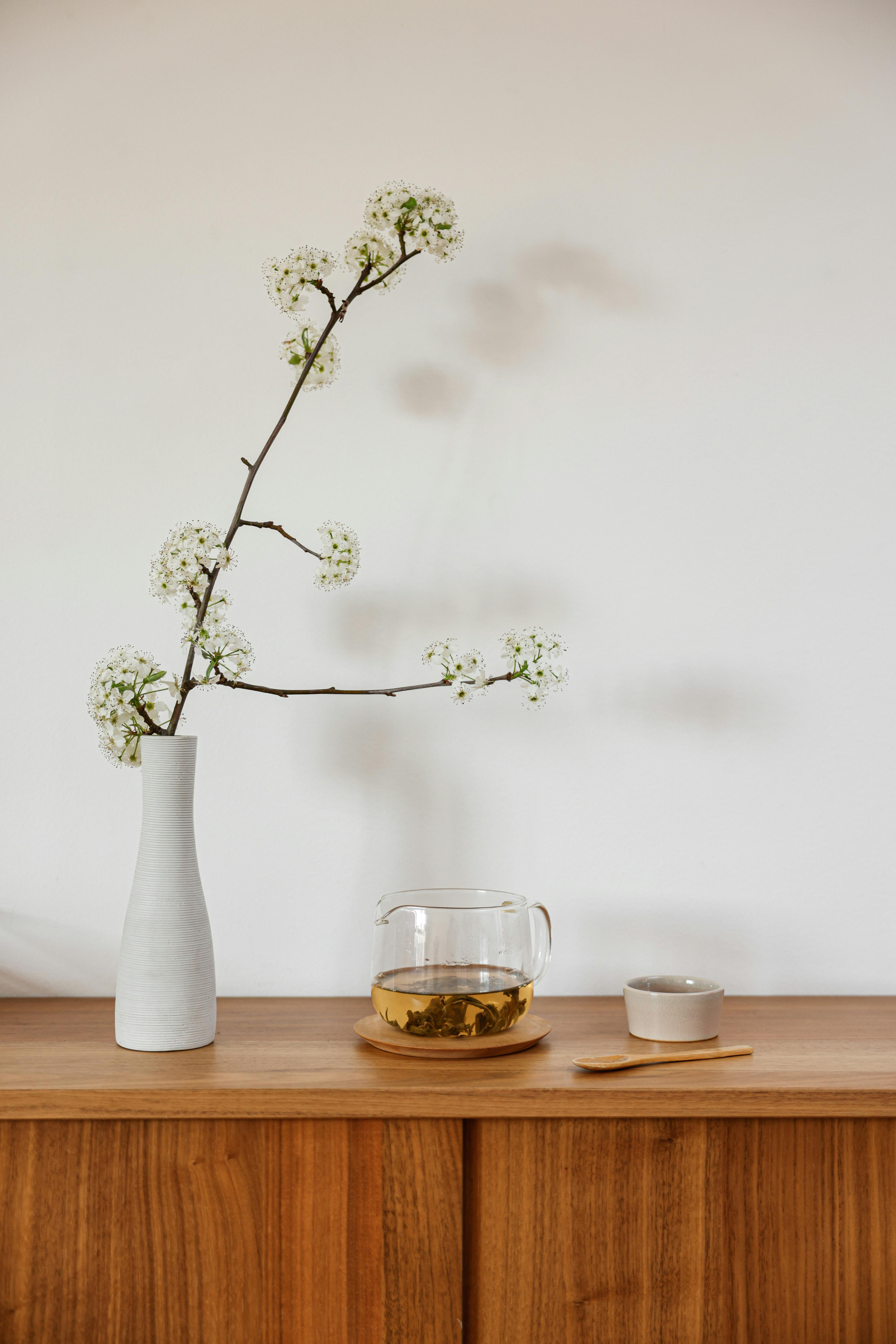 A minimalist setup featuring a vase with flowers and a tea set against a white wall.