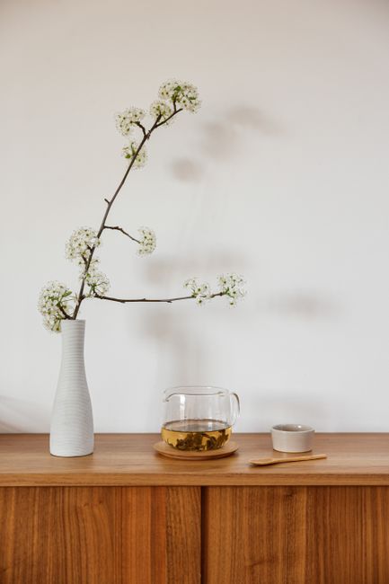 A minimalist setup featuring a vase with flowers and a tea set against a white wall.