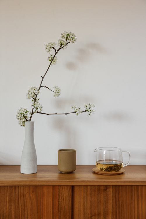 Free Elegant minimalist setup with a glass cup of tea and floral vase on a wooden cabinet. Stock Photo
