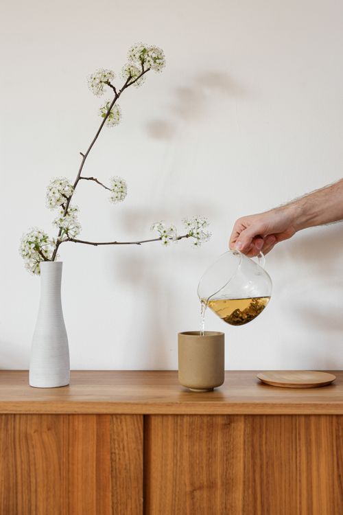 Free Elegant tea pouring next to a white floral arrangement on a wooden table. Stock Photo