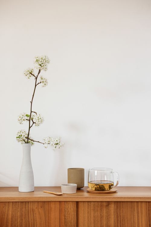 Free A minimalist scene with a white vase, flowering branch, and glass teapot on wood. Stock Photo