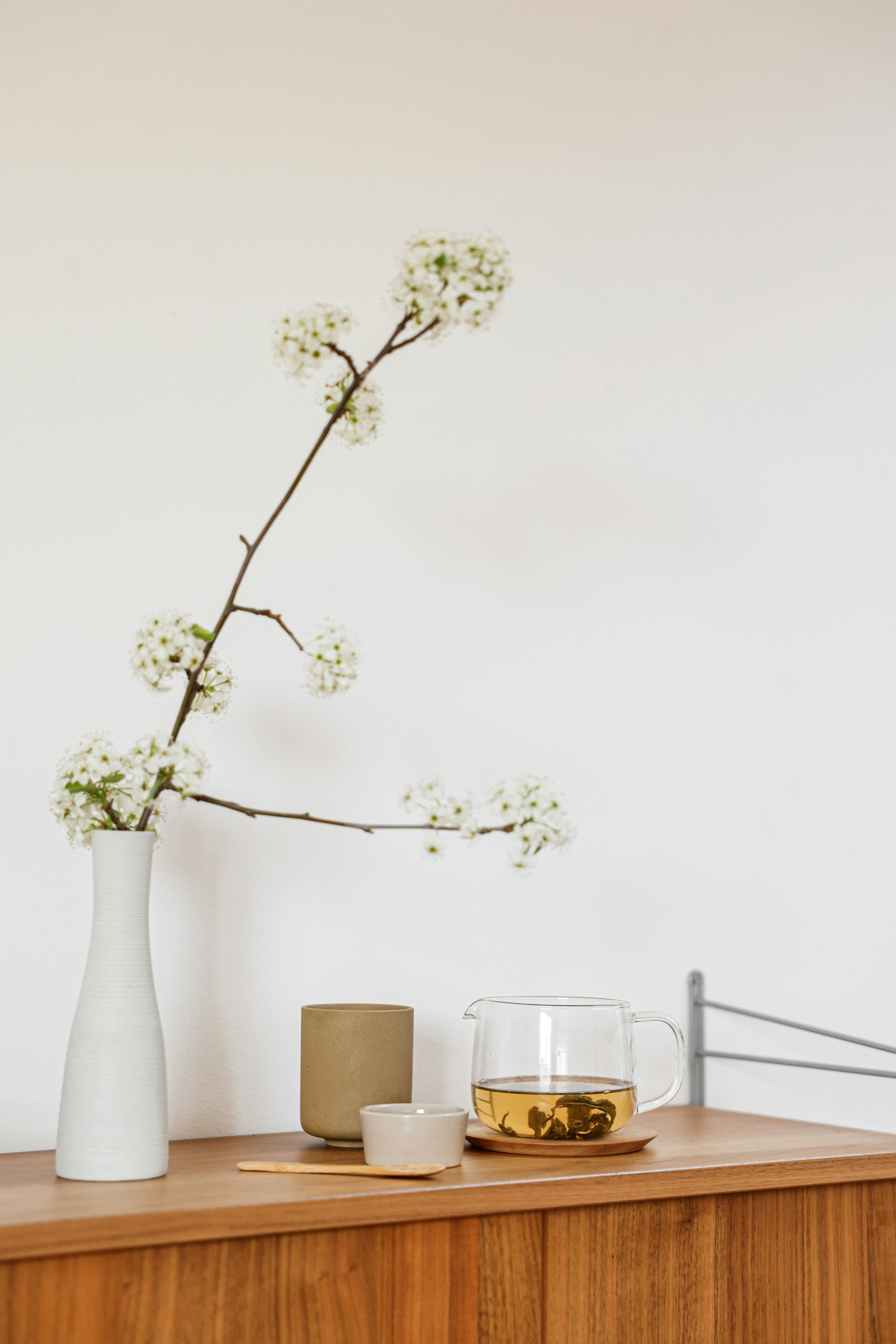 still life with a fruit tree branch with white flowers and tea on cupboard