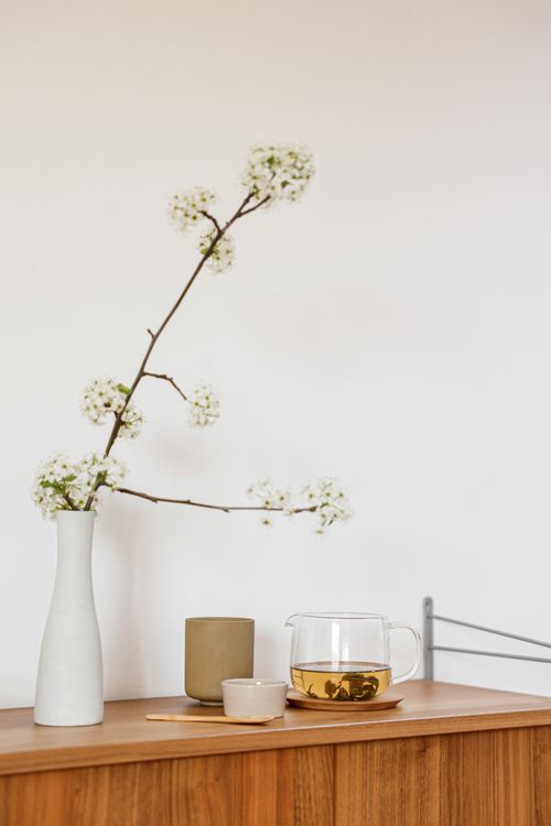 Free A serene minimalist setup featuring a blooming branch in a vase and a tea set on a wooden surface. Stock Photo