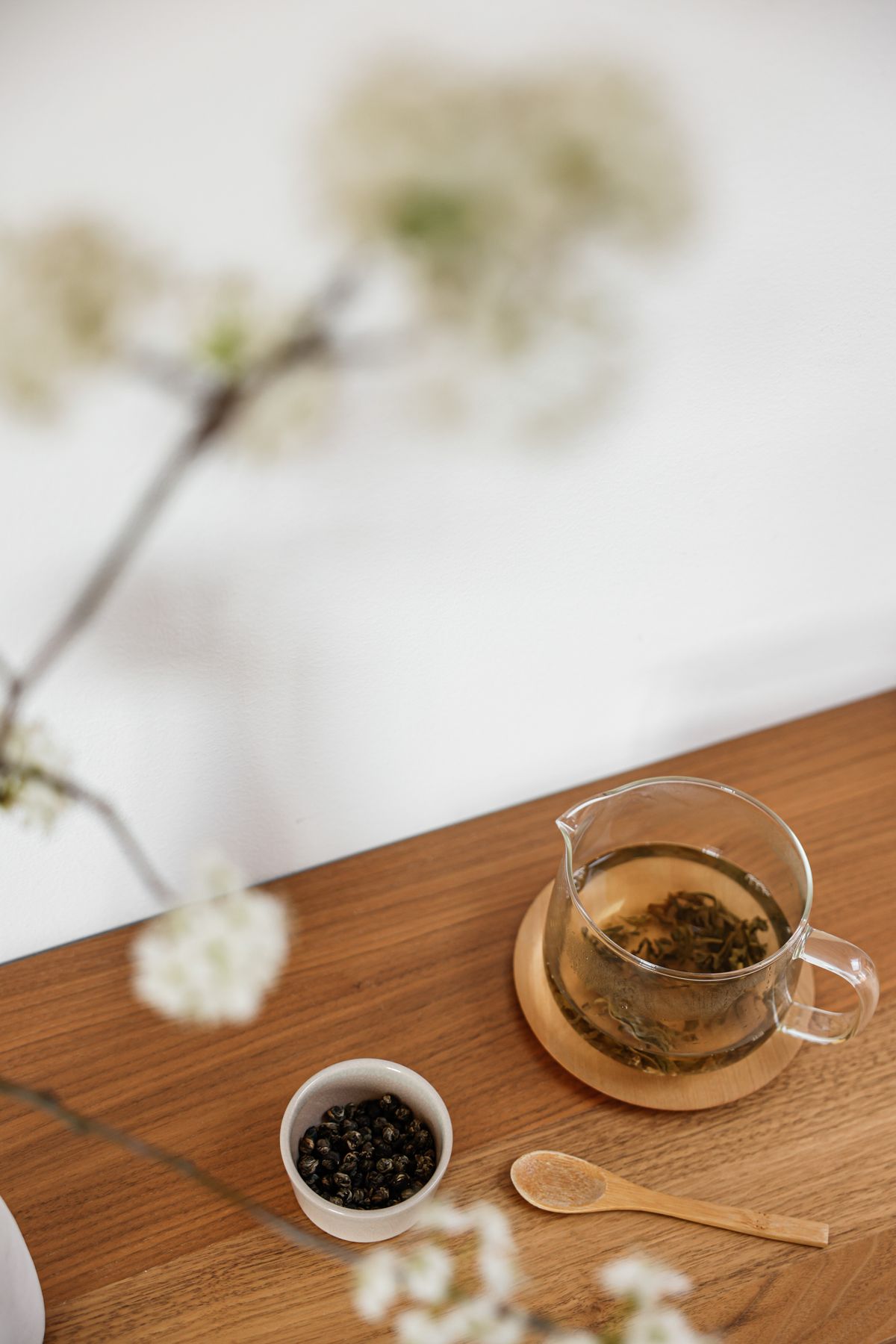 A glass teapot with tea leaves, flowers, and a wooden spoon