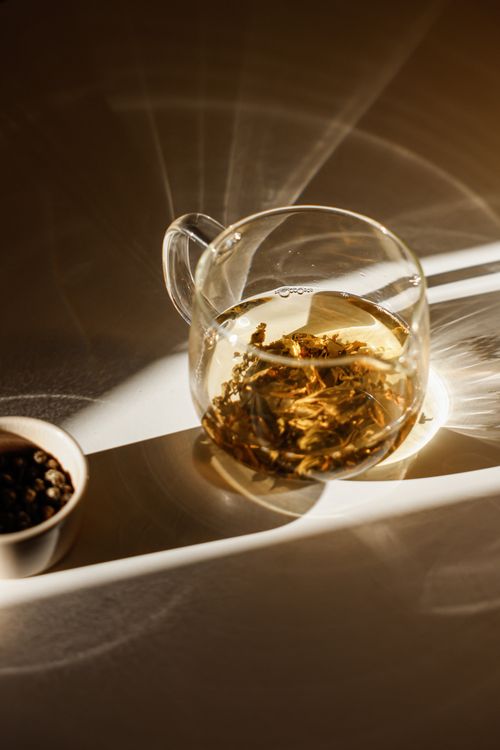 Free A beautifully lit glass teapot filled with tea leaves casting artistic shadows. Stock Photo