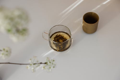 Herbal Tea in Glass Container Beside a Ceramic Cup