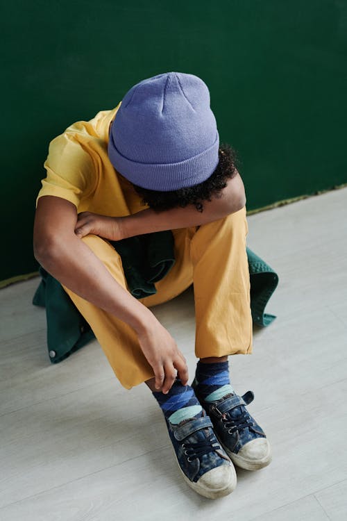 Boy in Yellow T-shirt and Purple Beanie Sitting on Floor with Head Down