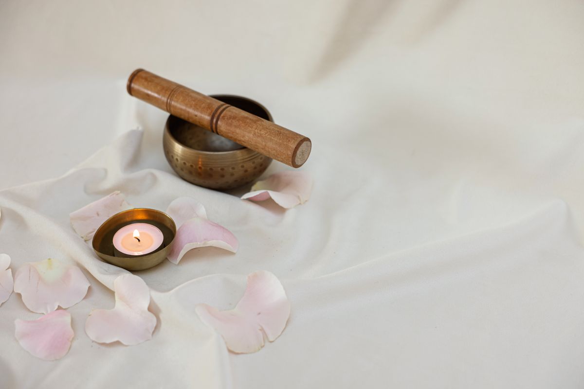 Lighted candle beside a singing bowl on a treatment table