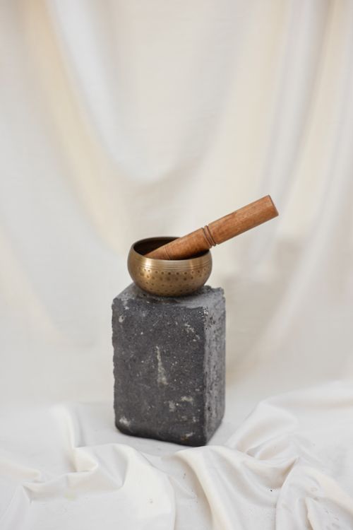 Free A serene essential still life featuring a brass singing bowl with wooden mallet on a rustic pedestal. Stock Photo