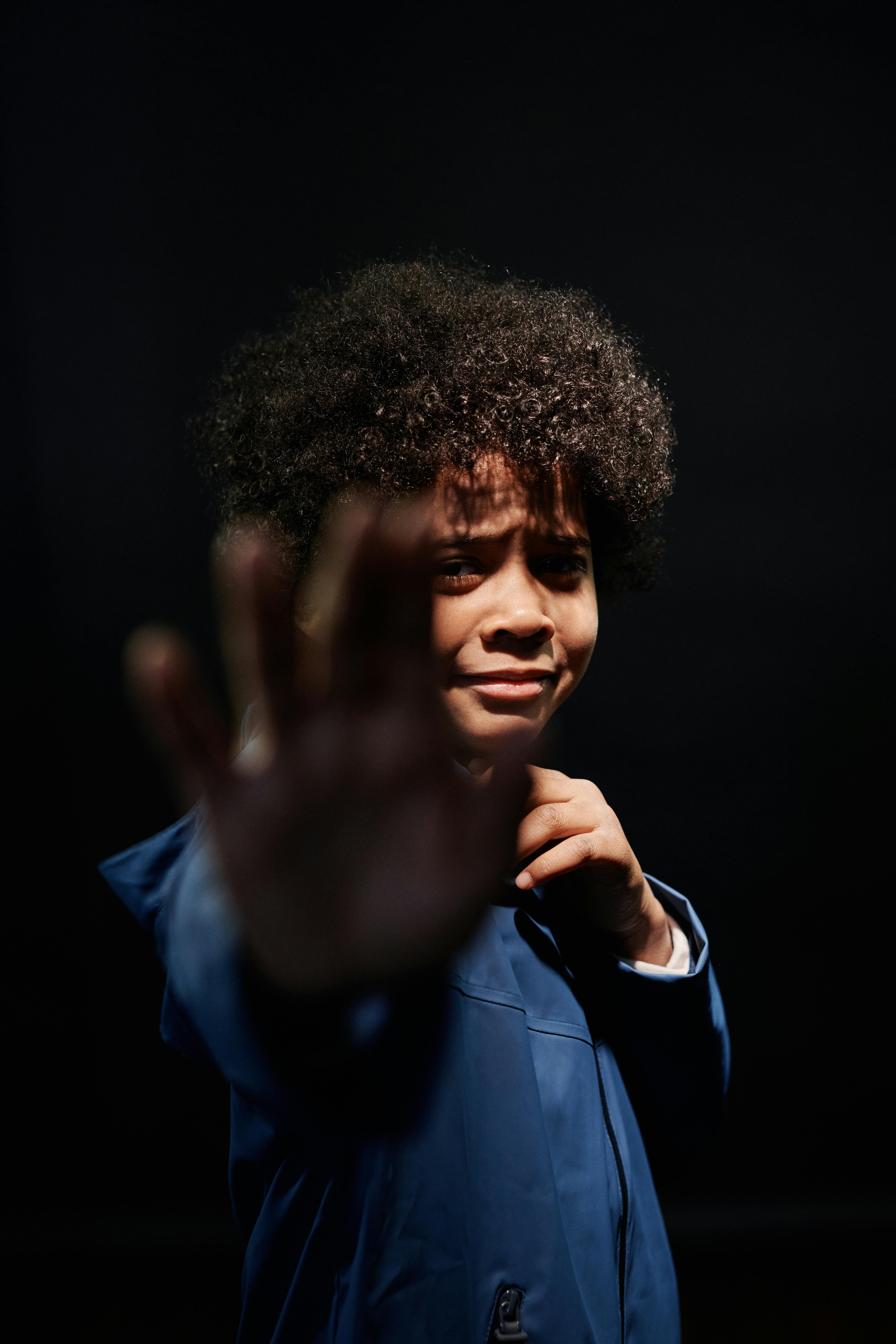 A child with afro hair in a blue jacket, captured in a dramatic shot with emotional expression.
