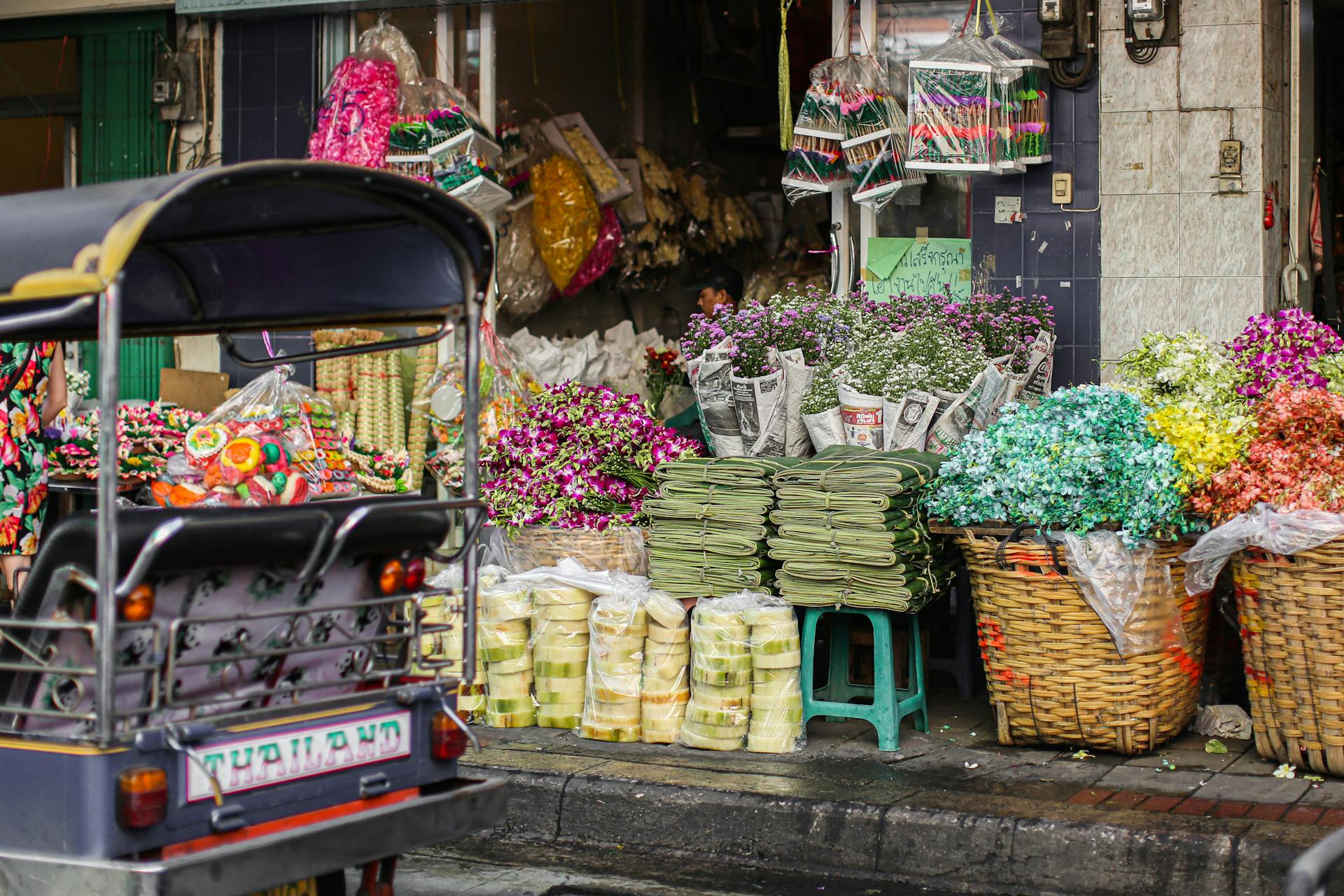 Bustling flower market stall in Bangkok with vivid blooms and a tuk-tuk in view.