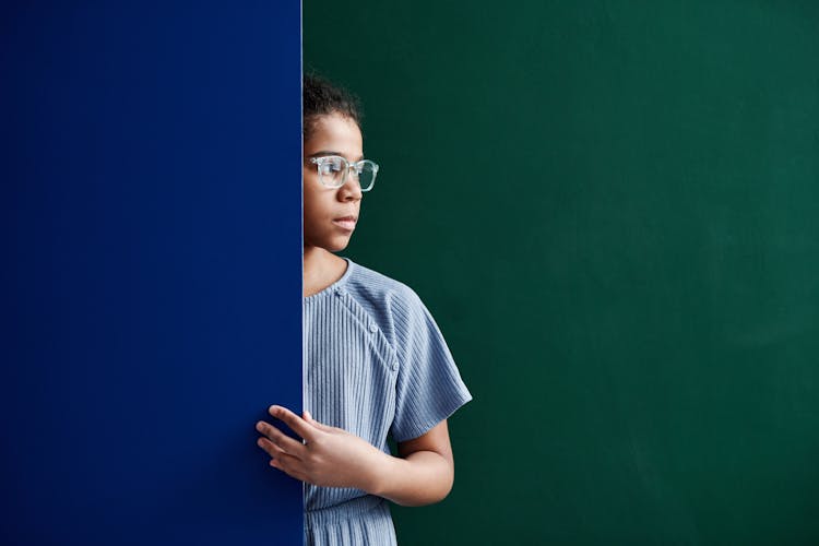 A Woman In Blue Shirt Standing Between Green And Blue Wall