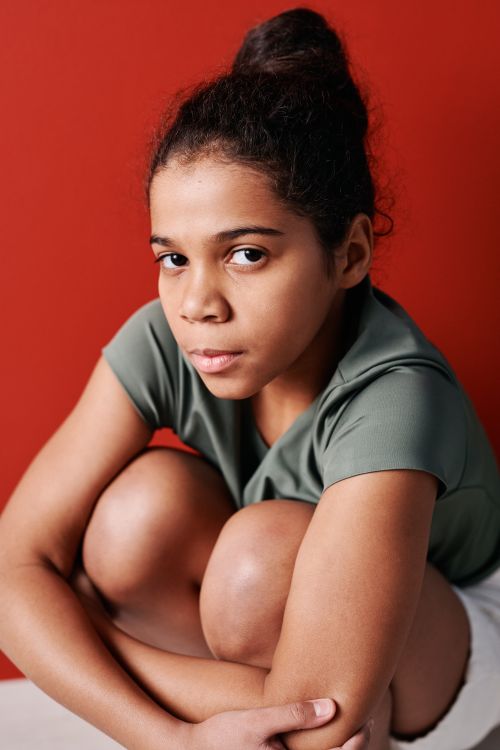 Free Close-up portrait of a young girl in a studio with a vivid red backdrop, depicting introspection. Stock Photo