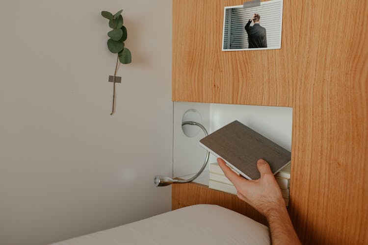 A Person Putting A Book In A Shelf