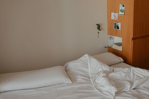 Free A minimalist bedroom featuring an unmade bed with white sheets and wooden decor. Stock Photo
